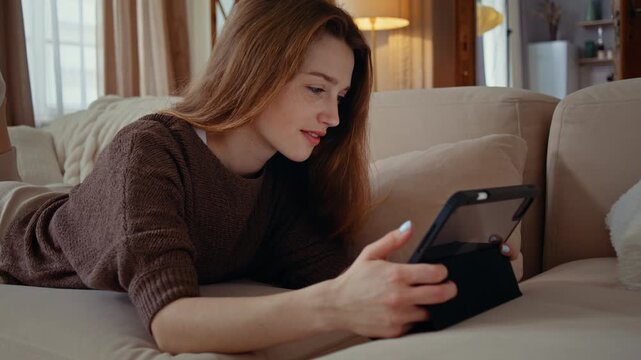 Young woman watches tablet on sofa in relaxed pose at home