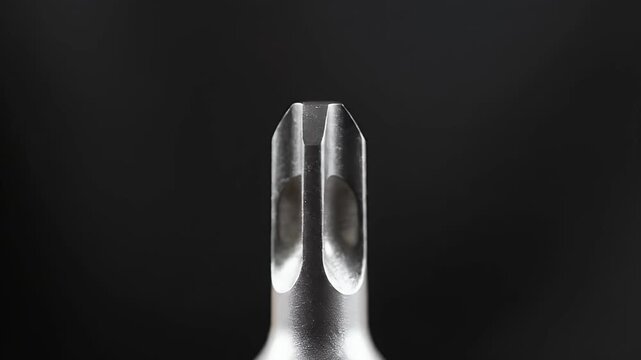 A detailed close-up shot of a sharp, silver-colored screwdriver bit stands out against a dark, contrasting background.