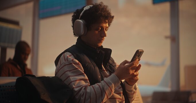 During Warm Golden Hour, Male Passenger Managing Travel Logistics. After Putting on Silver Headphones, Man Cross References Boarding Pass With Mobile App on Smartphone. Travel Apps, Airline Marketing.