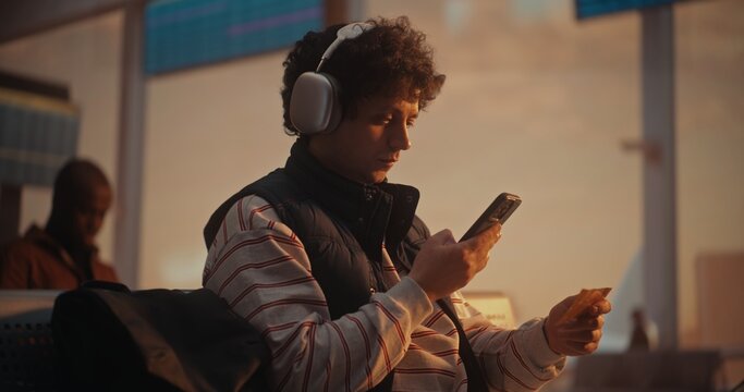 During Warm Golden Hour, Male Passenger Managing Travel Logistics. After Putting on Silver Headphones, Man Cross References Boarding Pass With Mobile App on Smartphone. Travel Apps, Airline Marketing.