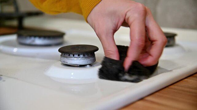Hand scrubbing gas stove burners with sponge in bright kitchen setting