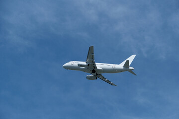 Obraz premium White passenger airplane climbing in the blue sky with light cirrus clouds after takeoff. White aircraft taking off and gaining altitude against a beautiful blue sky and wispy clouds.