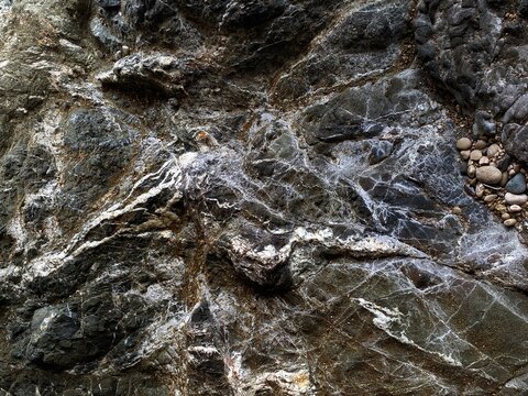 The texture of a dark stone is a close-up. Cliffs on the shores of the Mediterranean Sea in Camyuva, near Kemer, Turkey. A white pattern on a dark stone.