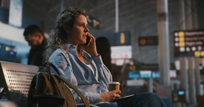 Young Woman Sits Comfortably In Airport Lounge, Enjoying Coffee While Having Cheerful Phone Conversation. Stress Free Travel Experience, Positive Emotions, and Staying Connected With Loved Ones.