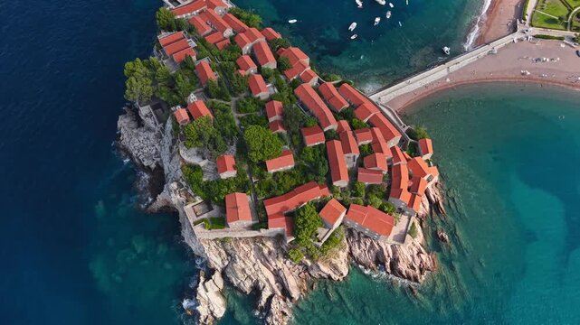 Aerial view of Sveti Stefan island's terracotta rooftops against the turquoise sea, linked by a narrow isthmus, Sveti Stefan, Budva Municipality, Montenegro.