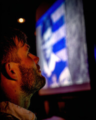 Bearded man profile with orange glow watches blurred screen in dark