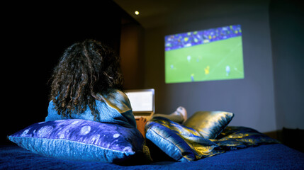 Person watching football game on wall from bed in dimly lit room