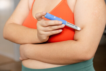 A horizontal medium shot of an young woman giving an injection to her forearm A young woman giving an injection of semaglutide to her shoulder  © Oleg