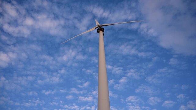 Timelapse view of a wind turbine filmed from below, with blades rotating against a sky filled with fast moving clouds. Strong perspective and dynamic motion highlight renewable energy, technology 