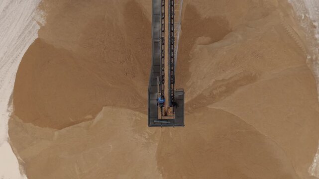 Aerial view of tan industrial material and a metal conveyor belt, creating a stark contrast of textures and tones, Arsoli, Lazio, Italy.