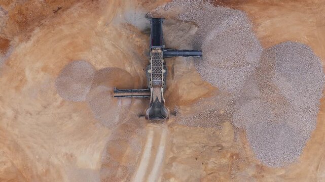 Aerial view of a quarry site where a loader and machinery contrast against the light brown earth and piles of rocks, Arsoli, Lazio, Italy.
