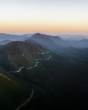 Aerial view of Mt Terminio with a winding mountain road snaking through lush green slopes under a soft sunset sky in Serino, Campania, Italy.