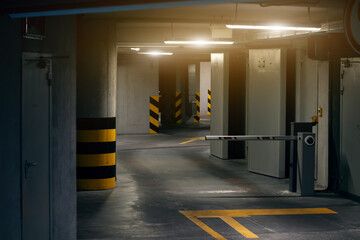 A dimly lit parking garage with a barrier arm and yellow markings on the floor and pillars © Artem Kniaz
