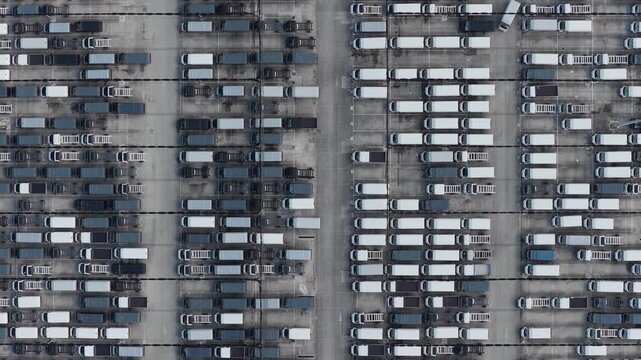 Aerial view of orderly rows of parked vans, a sea of white and grey vehicles creates a geometric pattern on the concrete, Atessa, Abruzzo, Italy.