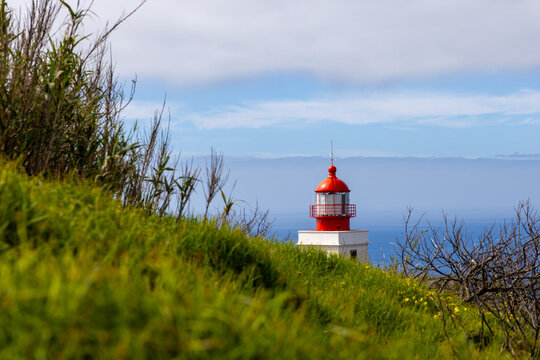 View of the red tip of a lighthouse seen from a hill with mist over the sea