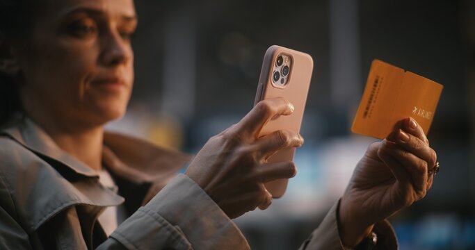 Young Woman in Airport Terminal, Carefully Cross Referencing Data Between Paper Ticket and Phone. Organization, Travel Planning, and Reliability of Digital Check in Services in Modern Aviation.