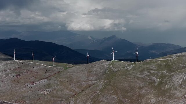 Aerial view of the wind turbines standing tall atop the hill with mountains in the background, Cocullo, Abruzzo, Italy.