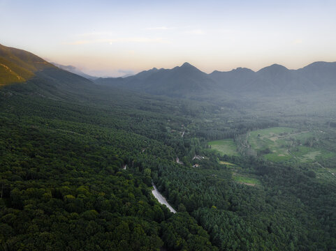 Aerial view of Mount Terminio featuring dense green forests and a winding road through the valley in Sala, Campania, Italy.