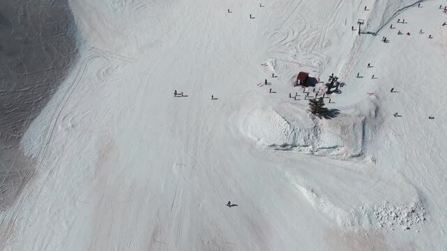 Aerial view of skiers dotting the pristine white slopes of a ski resort in Piano Provenzana, with a vibrant red building nestled amongst the snow, Piano Provenzana, Italy.