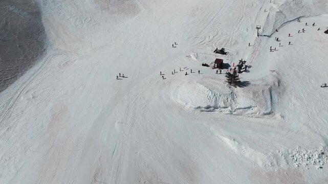 Aerial view of snowy slopes with scattered skiers and a ski lift station in Piano Provenzana, offering a winter wonderland scene, Piano Provenzana, Sicilia, Italy.