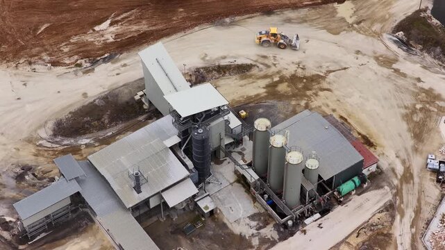 Aerial view of an industrial site with tanks, buildings, and a yellow construction vehicle, contrasting with the surrounding terrain, Magliano de' Marsi, Italy.