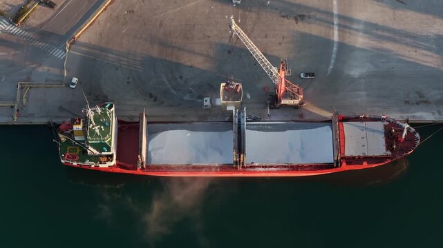 Aerial view of a cargo ship being loaded at the dock, contrasting the ship's red hull with the dark water, Vasto, Abruzzo, Italy.