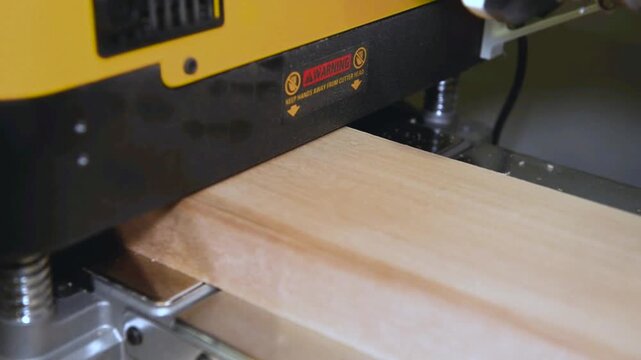A wood plate passing through the thickness planer machine in a carpentry workshop. Woodworking process, furniture preparation, handmade craftsmanship, carpentry studio.