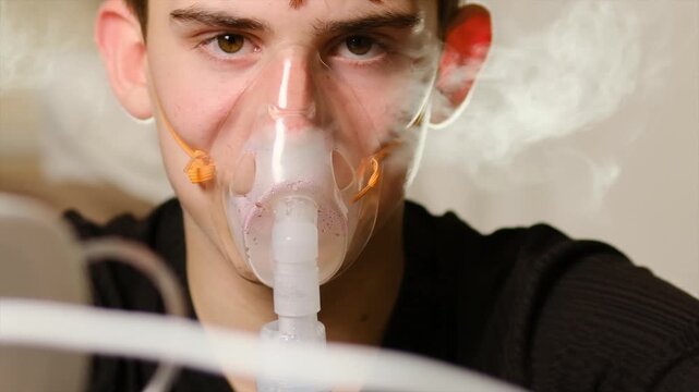 Teen boy inhalation process using face mask with medicinal mixture for treatment of bronchitis or pneumonia. Using compression nebulizer for lung problems. Hormonal medicines for bronchi