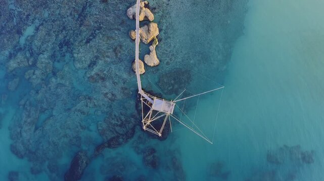 Aerial view of a fishing structure in water contrasting with the rocky seabed and the sandy beach, San Vito Chietino, Abruzzo, Italy.