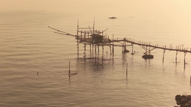 Aerial view of Trabocco, a wooden fishing structure stands in the tranquil sea during sunset, San Vito Chietino, Abruzzo, Italy.