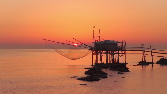 Aerial view of Trabucco at sunset with golden light reflecting on the sea, creating a warm and serene atmosphere, San Vito Chietino, Italy.