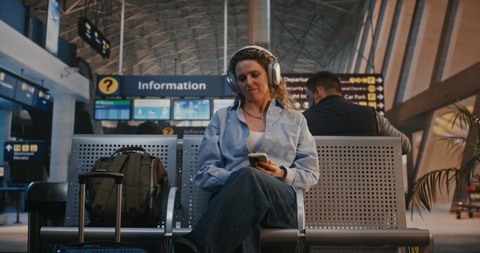 Female Traveler Scans Boarding Pass With Smartphone, Then Puts on Large Over Ear Headphones to Listen Music and Scroll Social Media. Concept of Digital Nomad Lifestyle and Youth Travel Culture.