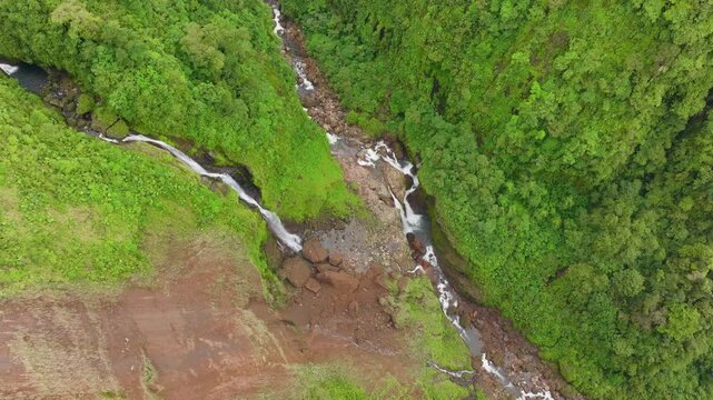 Aerial perspective of untouched rainforest waterfall in a remote part of Costa Rica, surrounded by dense jungle vegetation and dramatic green valley.