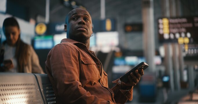 Sitting in Departure Lounge, Man Verifies Flight Details. Male Scans Ticket on Smartphone and Repeatedly Looks Up at Large Terminal Display Board FIDS to Cross Reference Gate Number and Boarding Time.