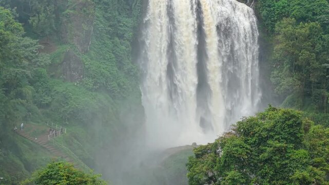 Aerial view of the majestic Curugsewu waterfall cascading down rocky cliffs amidst lush green foliage, creating a misty spectacle, Curugsewu, Central Java, Indonesia.