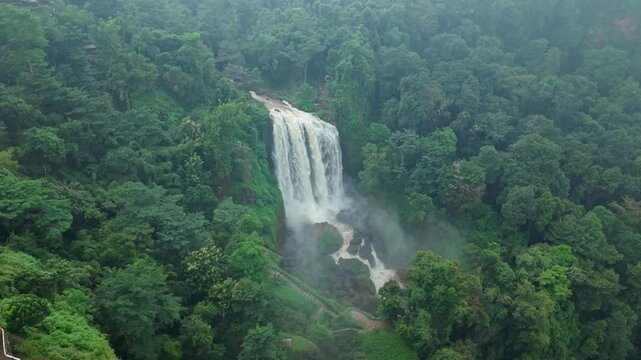Aerial view of the majestic Curugsewu Waterfall cascading down amidst a lush, vibrant green forest, creating a misty spectacle, Curugsewu, Central Java, Indonesia.