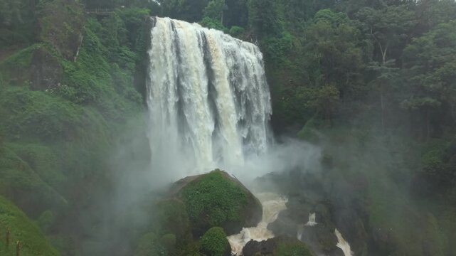 Aerial view of the majestic Curugsewu Waterfall cascading amidst lush green vegetation and misty surroundings, Kendal Regency, Central Java, Indonesia.