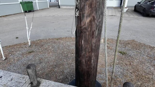 A weathered wooden mast fragment displayed as a decorative maritime element near a coastal building in Sweden. Coiled ropes wrap around aged timber, showing texture and wear. 