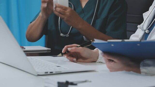 Medical team having a meeting with doctors in white lab coats and surgical scrubs seated at a table discussing a patients working online using computers
