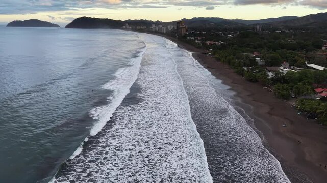 Aerial view of the dark sandy beach meeting the foamy turquoise ocean, with islands in the distance, creating a captivating contrast, Jaco, Costa Rica.