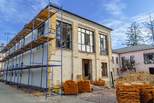 Reconstruction of a brick building damaged by combat. Blue scaffolding and construction materials for house restoration after military conflict