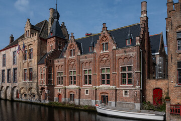 Fototapeta premium historic buildings on Dijver waterway canal, in Bruges city with boat. atmospheric image of Belgium