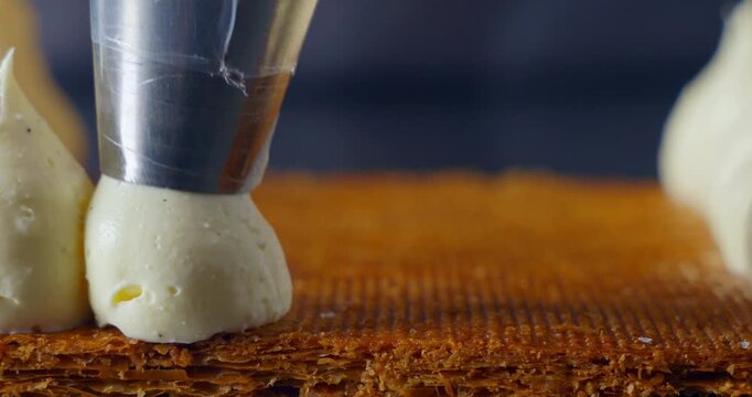 Close-up cinematic shot of a pastry chef decorating a cake with cream using a piping bag. Soft lighting enhances texture and precision.