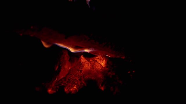 Close-up of a smoldering fire at night, creating a warm, inviting glow in the dark. Perfect for projects related to camping, survival, or creating a cozy atmosphere.