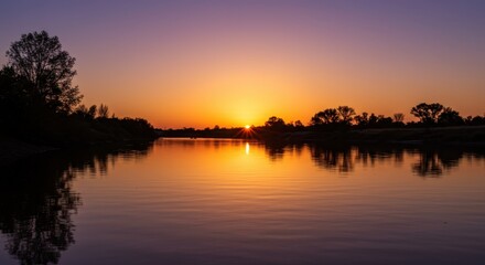 Fototapeta premium Fiery celestial body descends below the horizon casting warm reflections upon still water surfaces