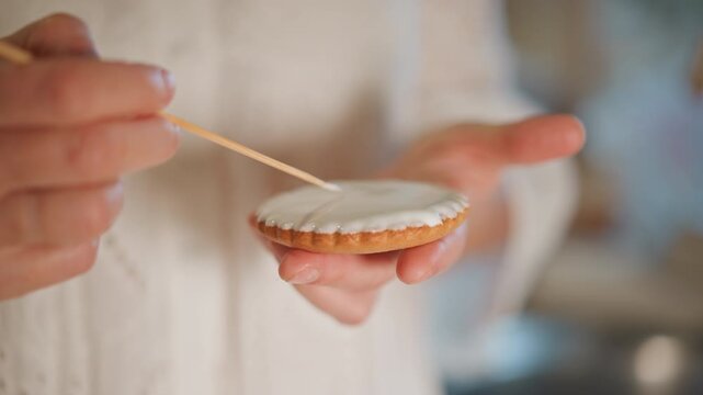 Closeup hand decorating pumpkin pie tart with icing using toothpick tool, delicate artisan technique in bright kitchen, smooth glaze and fingertip control, focus on texture and pattern, quiet precise