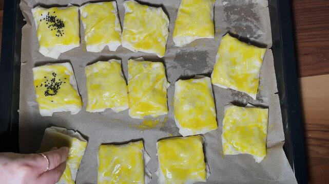 The stage of preparing the egg-filled pastries for the oven by sprinkling them with sesame seeds on the baking sheet. A traditional Turkish pastry recipe and homemade delicacies.