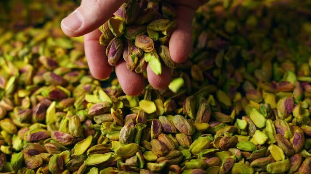Close-up cinematic shot of hands gently dropping pistachios onto other pistachios in slow motion. Soft lighting highlights texture and natural movement.