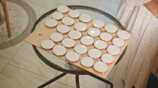 Tray mini pie shells on glass table, morning light casting soft shadows over neat rows of empty tart shells on baking board, round metal stand and tiled floor visible, curtain backdrop, warm neutral
