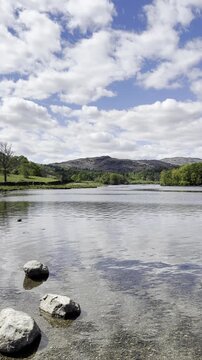 Lake shore video with stones in the foreground, gentle water surface and green hills in the background, Rydal Water, Lake District, England, UK.